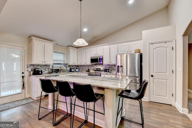 kitchen with appliances with stainless steel finishes, lofted ceiling, decorative backsplash, white cabinets, and a center island