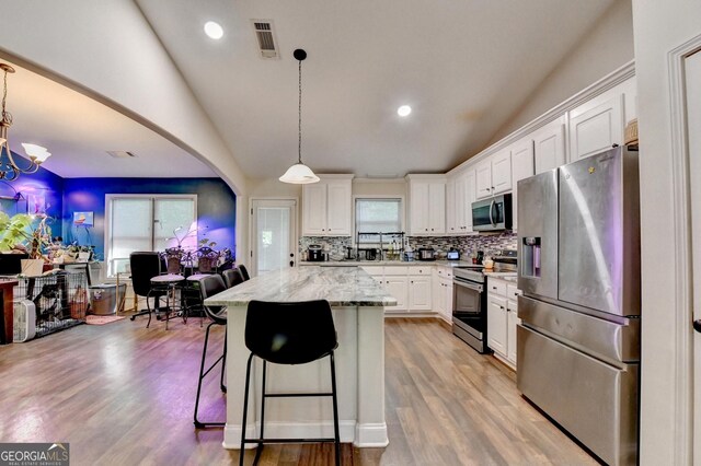 kitchen featuring appliances with stainless steel finishes, white cabinetry, tasteful backsplash, light wood-type flooring, and vaulted ceiling