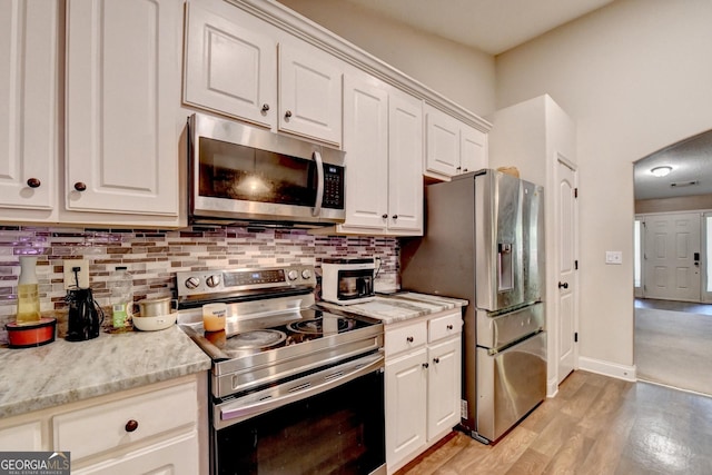 kitchen featuring stainless steel appliances, decorative backsplash, white cabinetry, and light wood finished floors