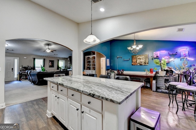 kitchen with arched walkways, a chandelier, light stone counters, decorative light fixtures, and dark wood-style floors