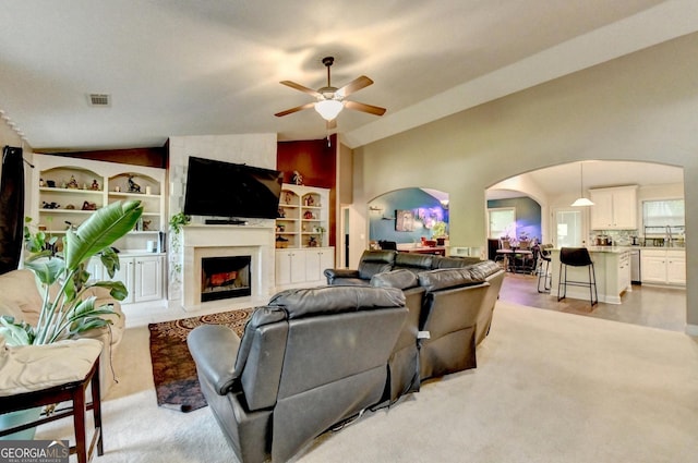 living room with arched walkways, lofted ceiling, a ceiling fan, a fireplace, and light carpet