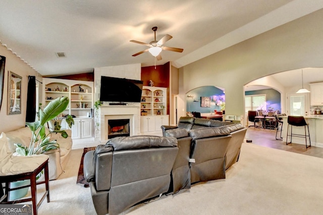 living room featuring vaulted ceiling, arched walkways, ceiling fan, a fireplace, and light carpet