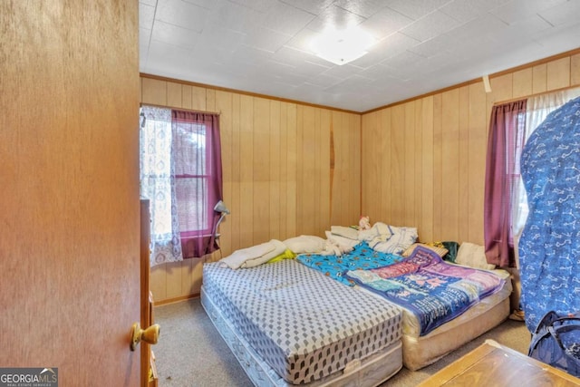 carpeted bedroom featuring ornamental molding, wooden walls, and multiple windows