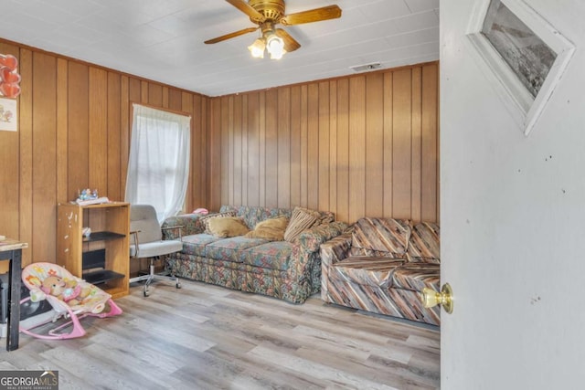 living area featuring a ceiling fan, wooden walls, visible vents, and wood finished floors