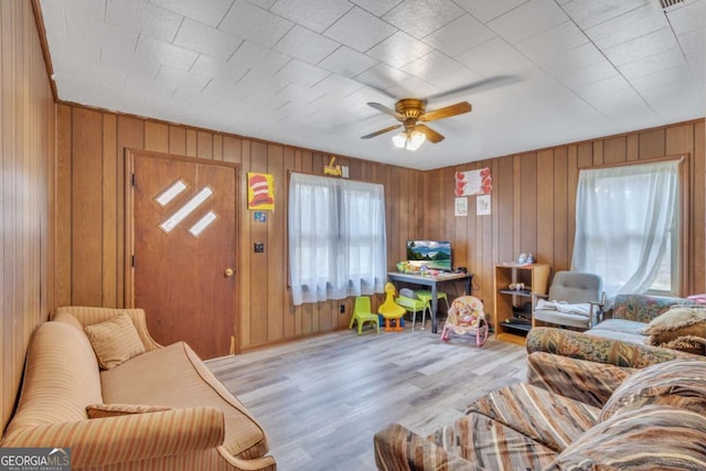 living room with light wood-style flooring, a ceiling fan, and wooden walls