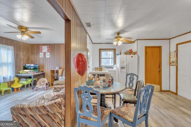 dining space with light wood-type flooring, visible vents, ceiling fan, and wooden walls