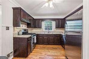 kitchen with appliances with stainless steel finishes, crown molding, dark brown cabinets, a ceiling fan, and light wood-style floors