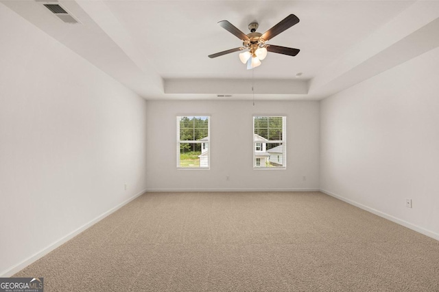 spare room featuring light colored carpet, visible vents, ceiling fan, a tray ceiling, and baseboards