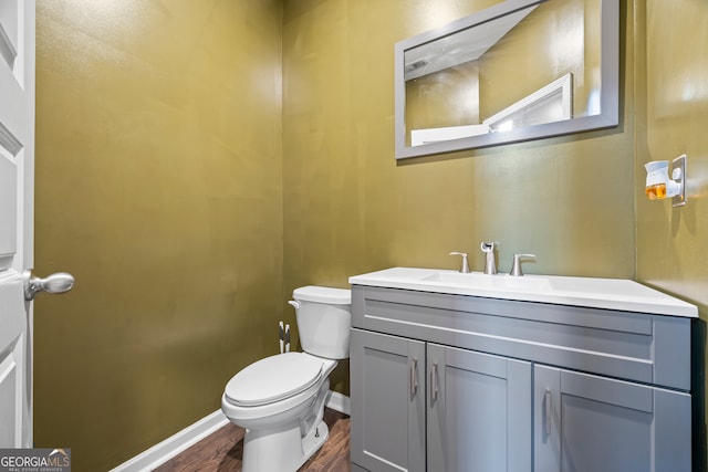 half bath with wood finished floors, baseboards, toilet, and vanity