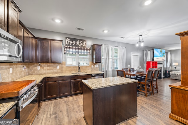kitchen with stainless steel appliances, a sink, a center island, dark brown cabinets, and decorative backsplash
