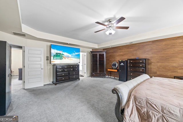 carpeted bedroom featuring wood walls and a ceiling fan