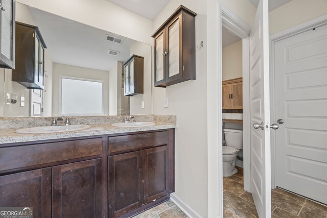 548 Azalea Bloom Dr E, Loganville, GA 30052 - bathroom featuring stone tile flooring, toilet, double vanity, and baseboards