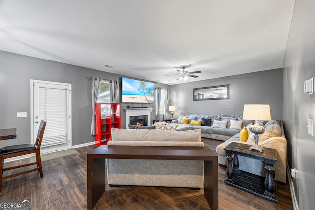 living room with ceiling fan, dark wood-style flooring, and a glass covered fireplace