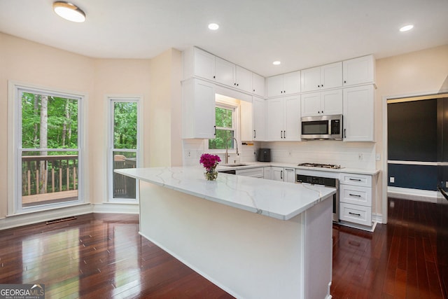 kitchen featuring oven, stainless steel microwave, light stone countertops, a peninsula, and dark wood-style flooring