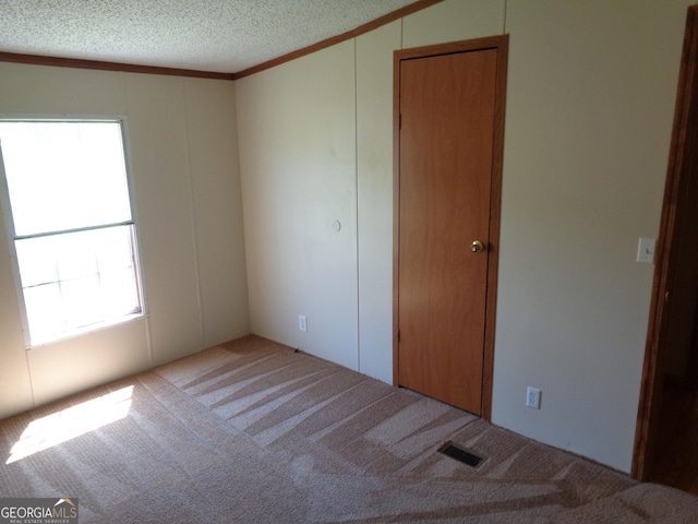 unfurnished room featuring a textured ceiling, carpet, ornamental molding, visible vents, and a decorative wall
