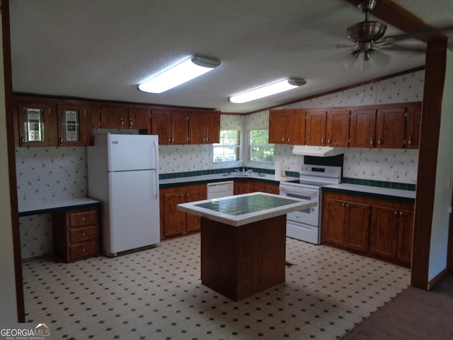 kitchen with lofted ceiling, under cabinet range hood, white appliances, a kitchen island, and tile counters
