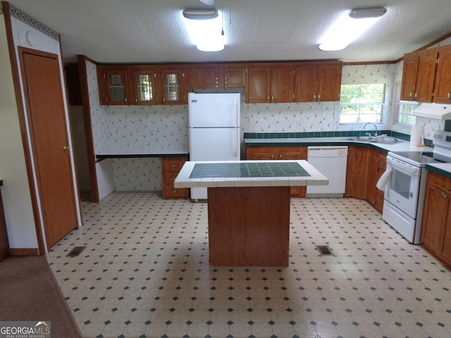 kitchen with under cabinet range hood, white appliances, a sink, a kitchen island, and tile counters