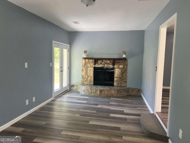 unfurnished living room featuring visible vents, wood finished floors, baseboards, and a stone fireplace