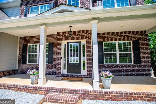 view of exterior entry featuring brick siding and a porch