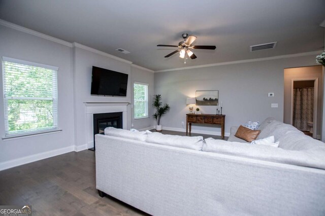 living room with ornamental molding, a ceiling fan, dark wood-style floors, a glass covered fireplace, and baseboards