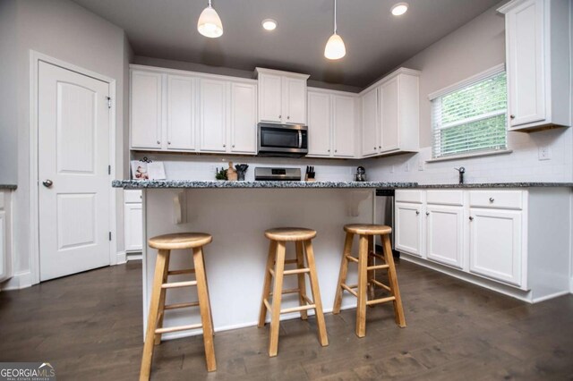 kitchen with stone counters, decorative light fixtures, a kitchen breakfast bar, white cabinets, and appliances with stainless steel finishes