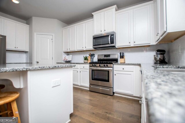 kitchen with stainless steel appliances, white cabinetry, dark wood-style floors, a kitchen bar, and recessed lighting
