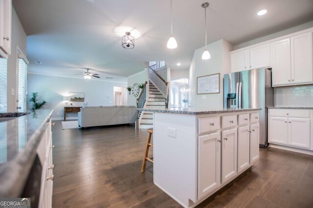 kitchen featuring stainless steel fridge with ice dispenser, a ceiling fan, white cabinets, backsplash, and a kitchen breakfast bar