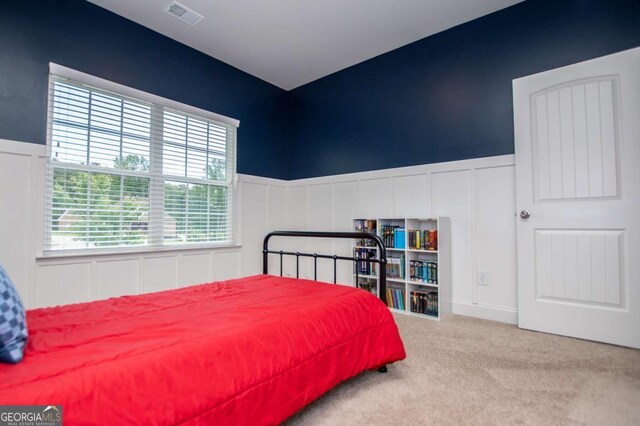 carpeted bedroom featuring a decorative wall and a wainscoted wall