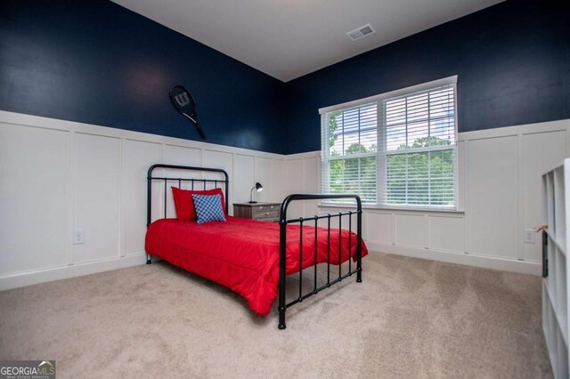 carpeted bedroom with a decorative wall and wainscoting