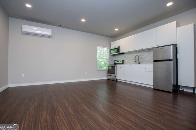 kitchen with appliances with stainless steel finishes, a wall mounted air conditioner, a sink, dark wood-style flooring, and white cabinets