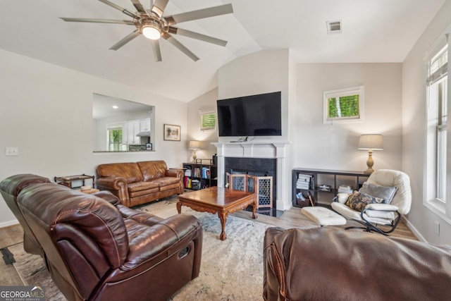 living room featuring a ceiling fan, vaulted ceiling, a fireplace with flush hearth, baseboards, and wood finished floors