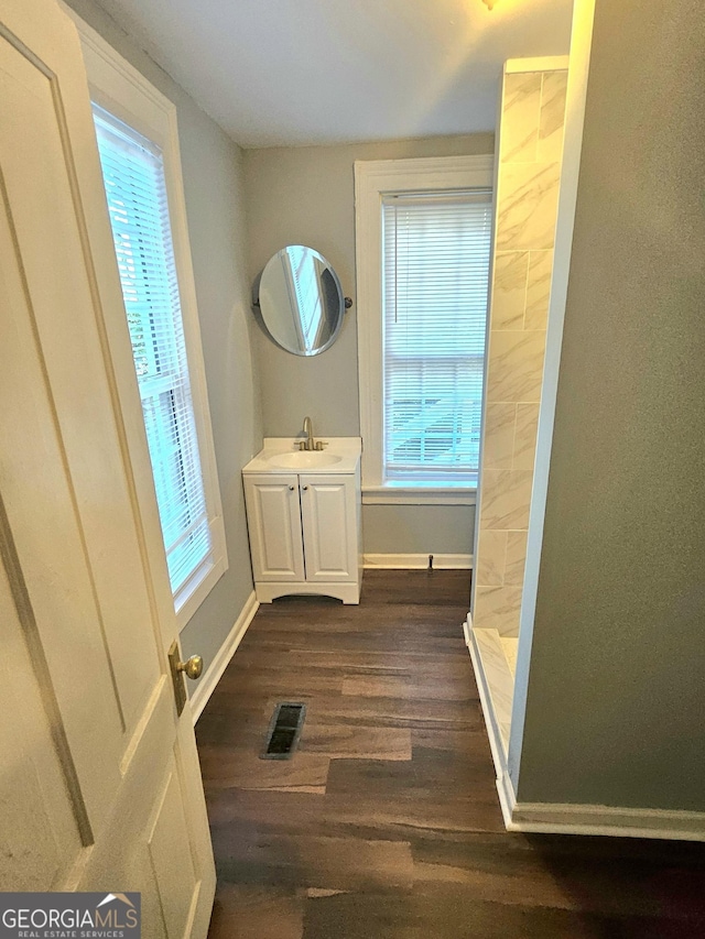 full bathroom with a tile shower, wood finished floors, vanity, and baseboards