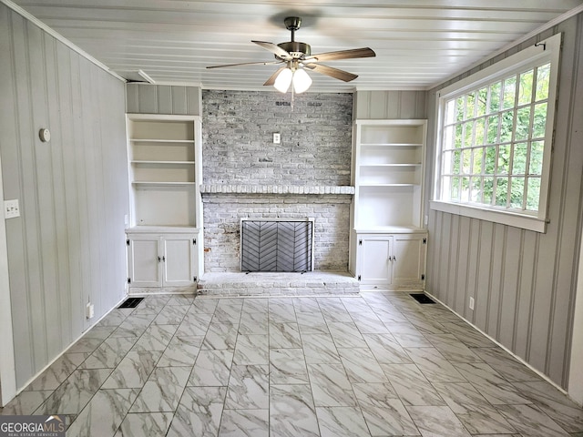 unfurnished living room featuring built in shelves, a ceiling fan, a fireplace, wood walls, and marble finish flooring