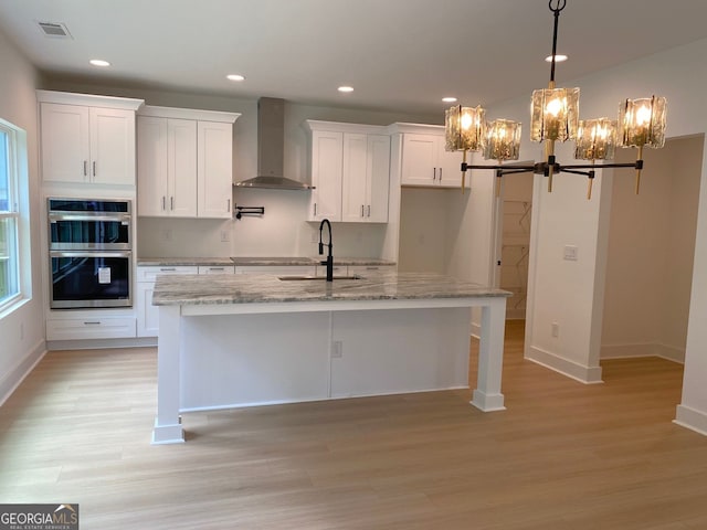 2167 Main St NW, Atlanta, GA 30318 - kitchen featuring wall chimney range hood, an island with sink, a chandelier, light wood finished floors, and white cabinetry