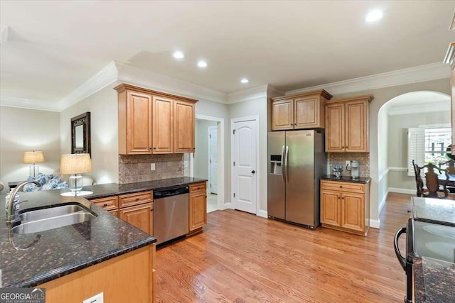 kitchen featuring appliances with stainless steel finishes, a sink, arched walkways, light wood-style flooring, and backsplash