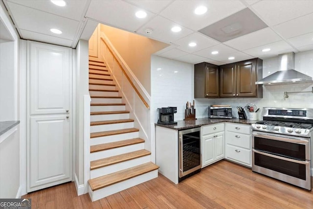 kitchen with appliances with stainless steel finishes, wall chimney exhaust hood, wine cooler, light wood-style flooring, and decorative backsplash