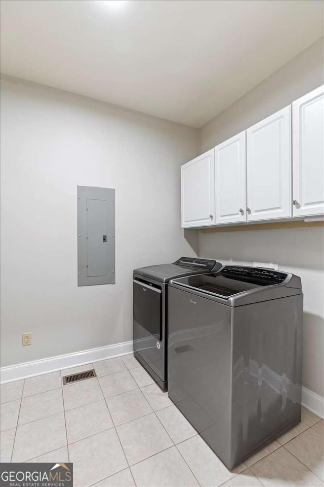 washroom with electric panel, cabinet space, washer and dryer, baseboards, and light tile patterned floors
