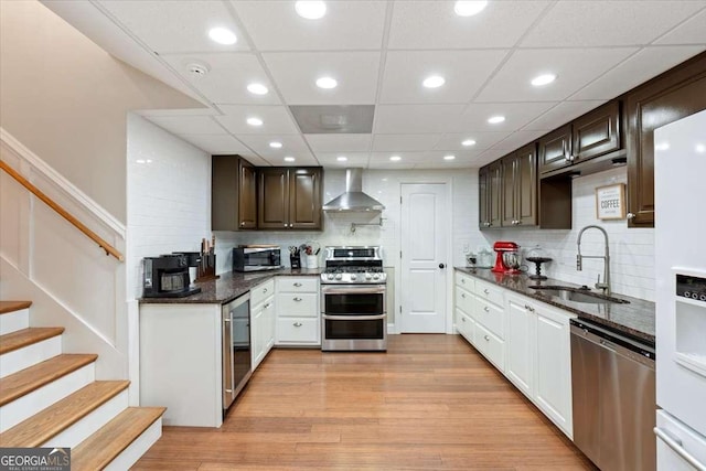 kitchen with a sink, appliances with stainless steel finishes, wall chimney range hood, dark brown cabinetry, and recessed lighting