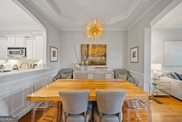 dining room featuring an inviting chandelier, light wood-type flooring, wainscoting, and crown molding
