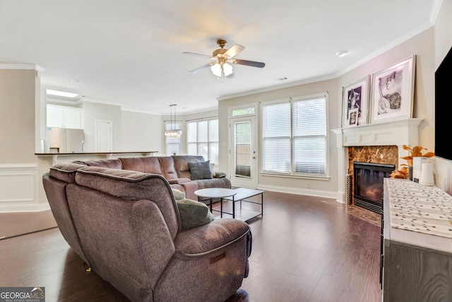 living area with ornamental molding, a tiled fireplace, ceiling fan, and dark wood-type flooring