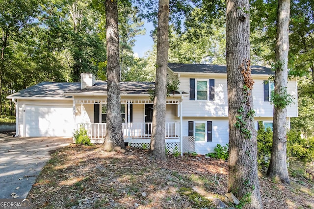 tri-level home with covered porch, a chimney, driveway, and an attached garage