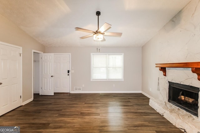 unfurnished living room featuring wood finished floors, visible vents, vaulted ceiling, ceiling fan, and a stone fireplace
