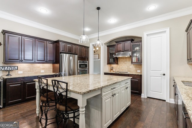 621 Oakbourne Way, Woodstock, GA 30188 - kitchen with appliances with stainless steel finishes, a center island, under cabinet range hood, dark brown cabinetry, and tasteful backsplash