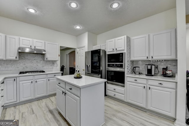 kitchen featuring white cabinets, black appliances, under cabinet range hood, light countertops, and tasteful backsplash