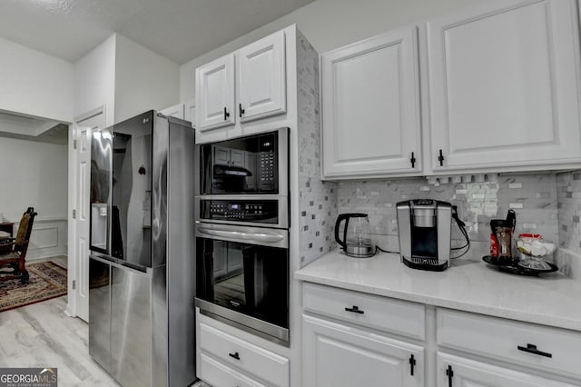 kitchen with backsplash, light wood-style floors, white cabinets, and appliances with stainless steel finishes