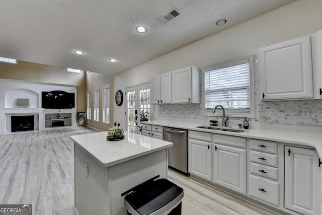 kitchen with a center island, dishwasher, light wood finished floors, a sink, and white cabinetry