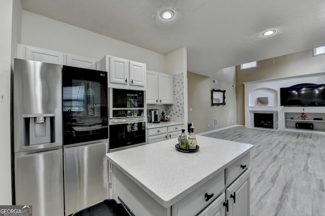 kitchen featuring light wood-style flooring, open floor plan, a center island, white cabinets, and appliances with stainless steel finishes