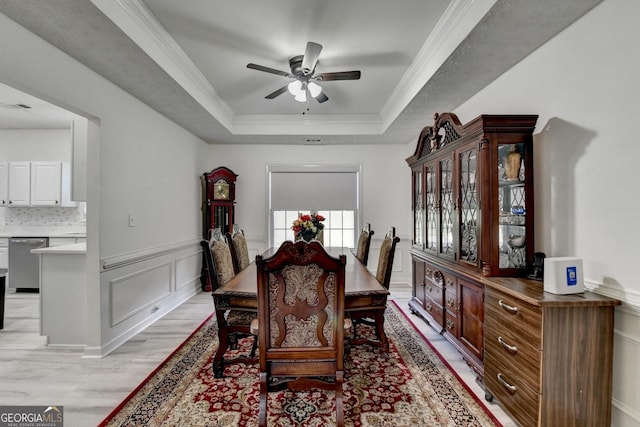 dining area with a wainscoted wall, a decorative wall, a raised ceiling, ceiling fan, and light wood-style floors