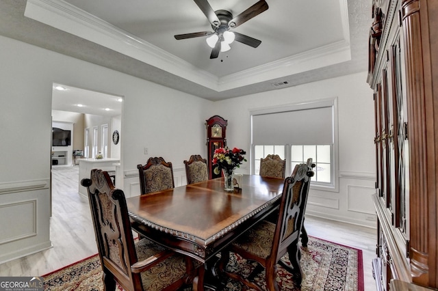 dining room featuring a raised ceiling, light wood-style floors, a decorative wall, and ceiling fan
