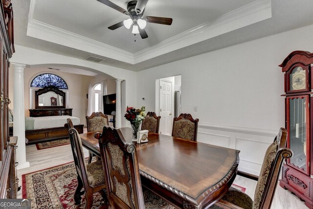 dining space with ornate columns, visible vents, arched walkways, a ceiling fan, and a tray ceiling